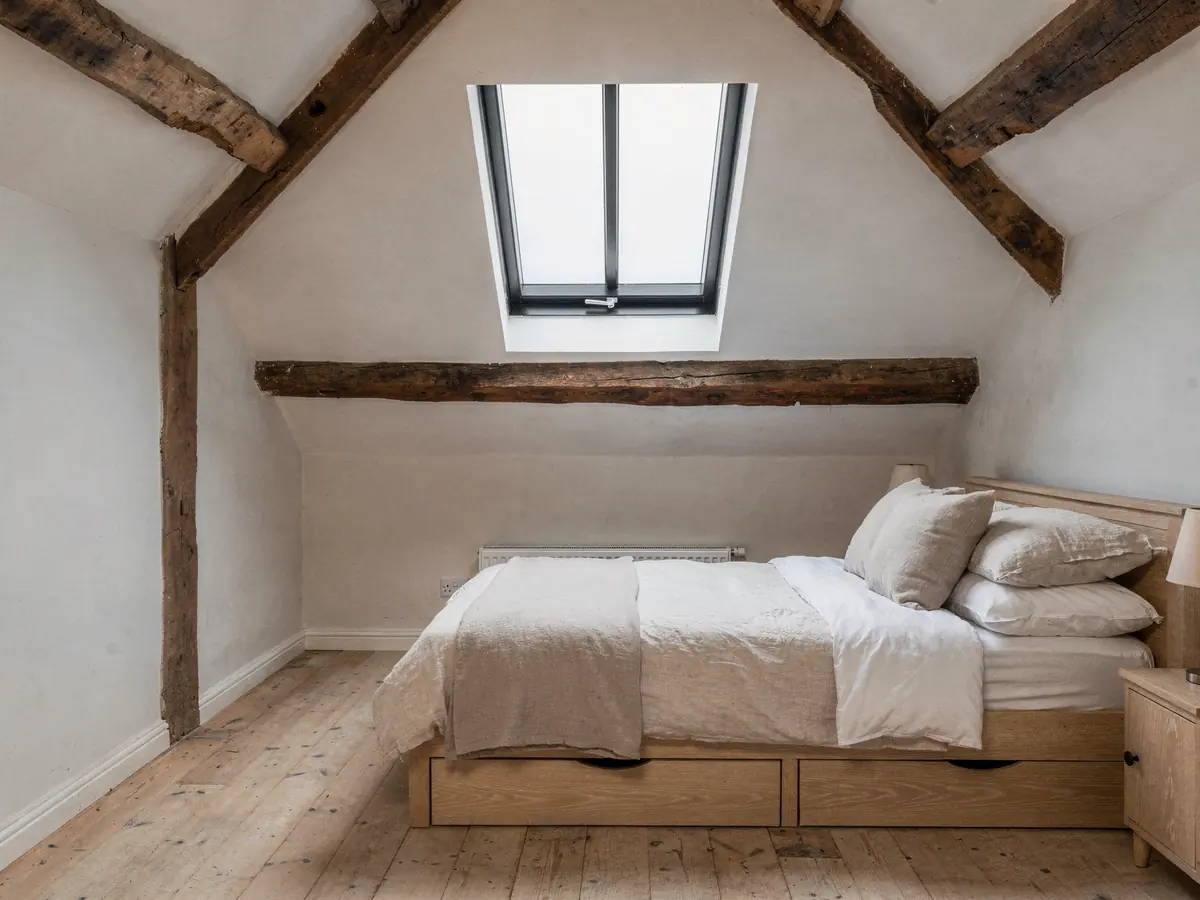 Cottage bedroom with exposed beams under a conservation rooflight